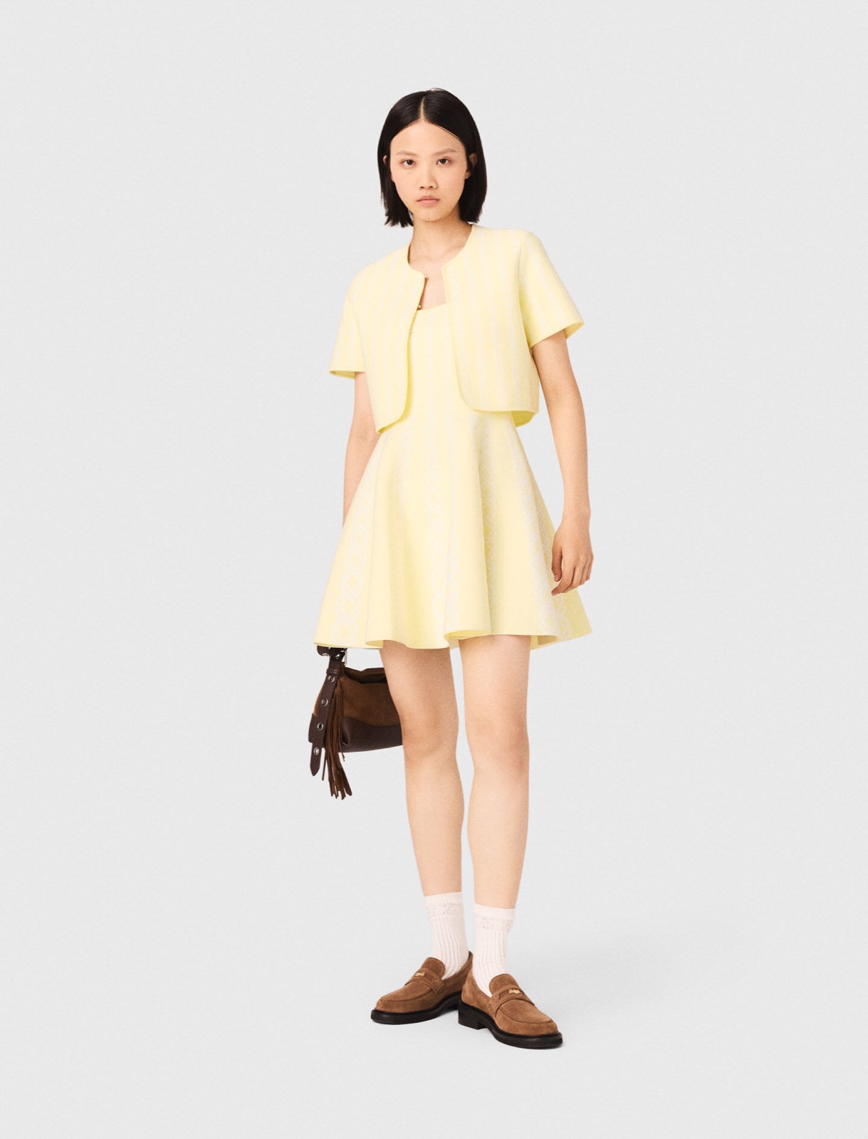 Veste courte en maille jacquard jaune pâle rayée de blanc, portée sur une robe assortie, signée Maje