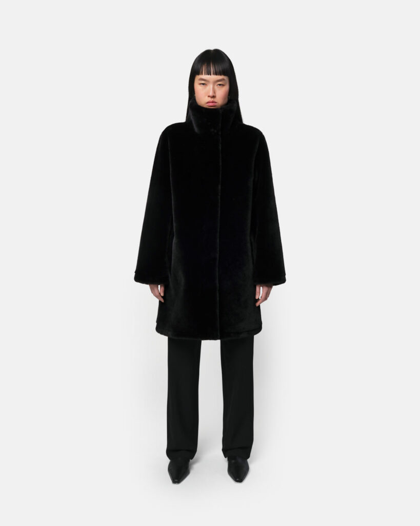 Manteau mi-long Blair en fausse fourrure noire d'Apparis, col montant, porté avec un pantalon droit noir