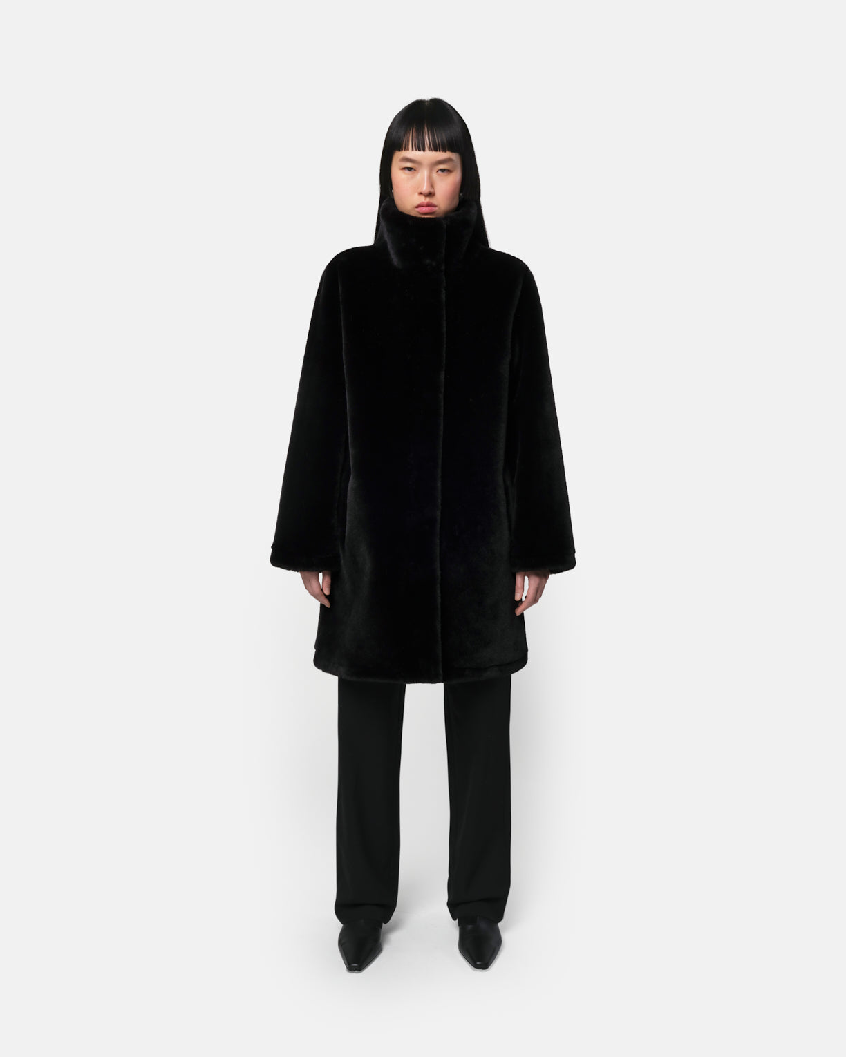 Manteau mi-long Blair en fausse fourrure noire d'Apparis, col montant, porté avec un pantalon droit noir