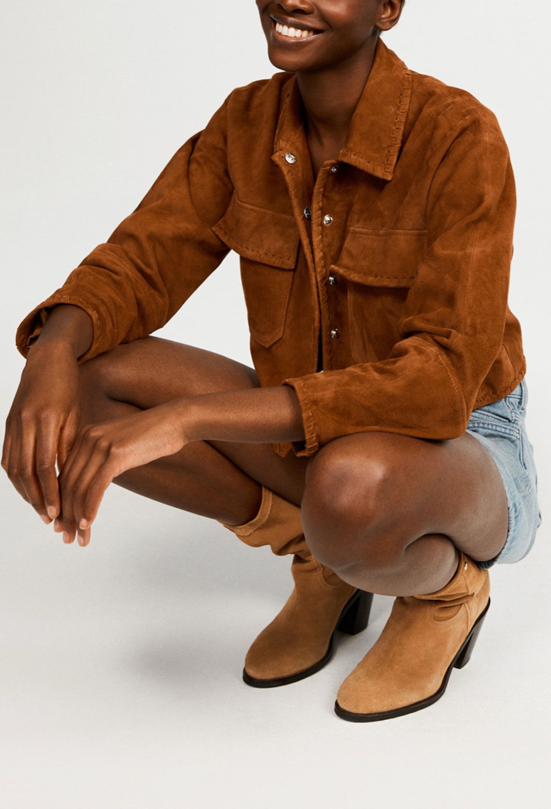 Blouson court en daim brun Cassis de Claudie Pierlot, boutons pression et poches poitrine, porté avec un short en jean