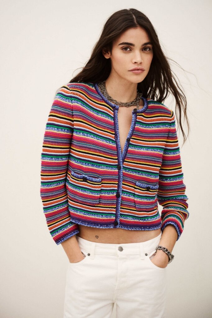 Cardigan Fanny de ba&sh, gilet en maille de coton à rayures multicolores, col rond et boutons, porté sur un jean blanc