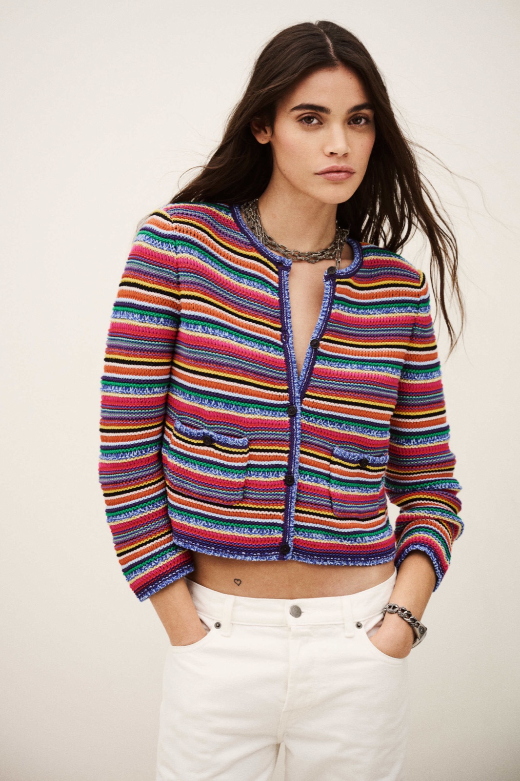 Cardigan Fanny de ba&sh, gilet en maille de coton à rayures multicolores, col rond et boutons, porté sur un jean blanc