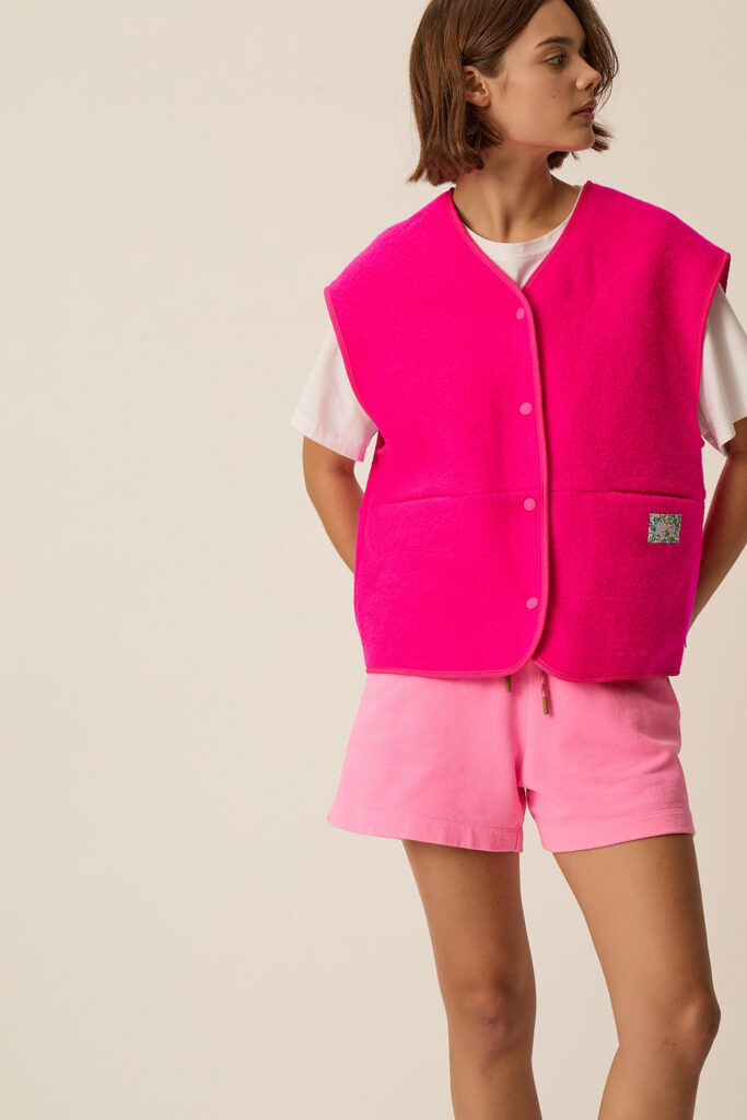 Gilet sans manches en maille bouclette de laine rose vif Gaelle de Des Petits Hauts, porté sur un tee-shirt blanc