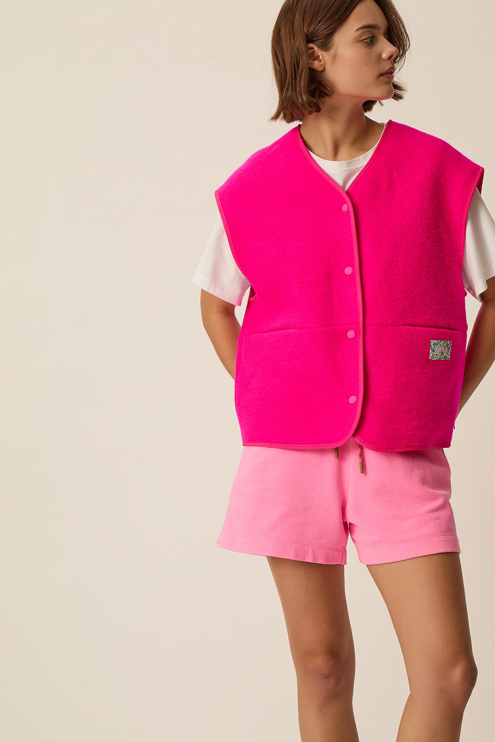 Gilet sans manches en maille bouclette de laine rose vif Gaelle de Des Petits Hauts, porté sur un tee-shirt blanc