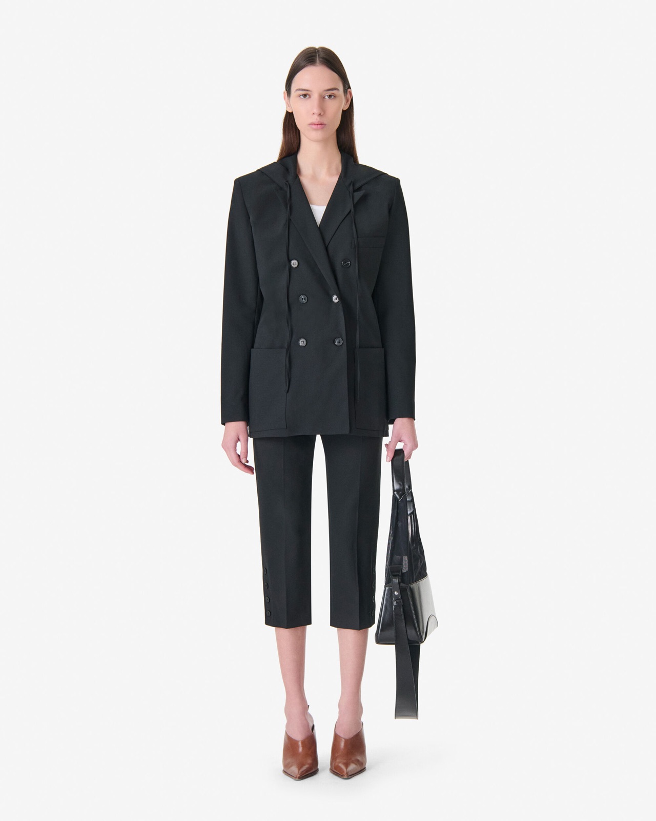 Veste de tailleur ALULA d'IRO en noir, coupe croisée avec capuche intégrée, portée sur un pantalon de tailleur noir