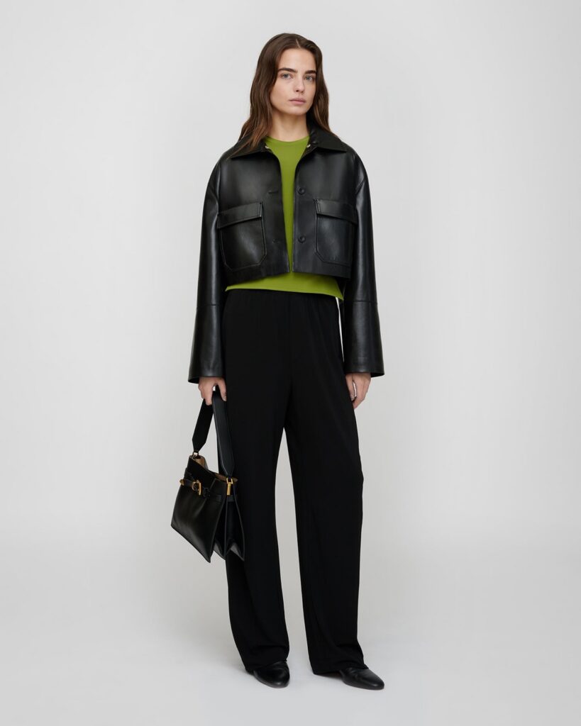 Veste courte Omolara de Nanushka en cuir vegan Okobor noir, portée sur un top vert et un pantalon fluide noir