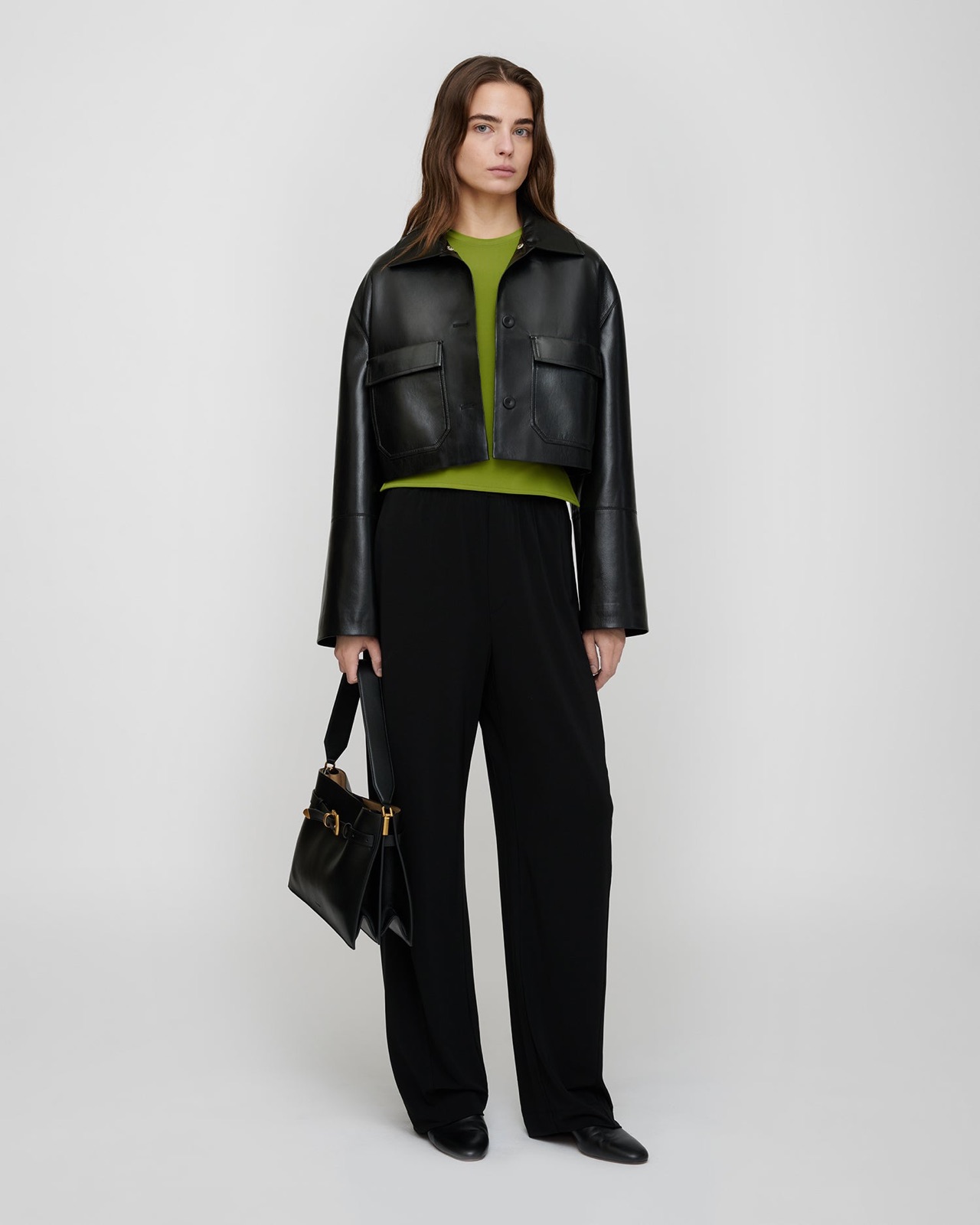 Veste courte Omolara de Nanushka en cuir vegan Okobor noir, portée sur un top vert et un pantalon fluide noir