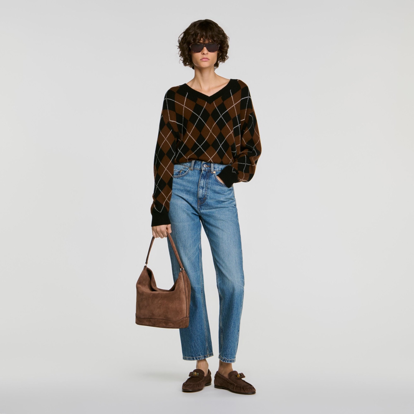 Pull en maille argyle à strass Sandro, motif losanges marron et noir, col V, porté avec un jean droit