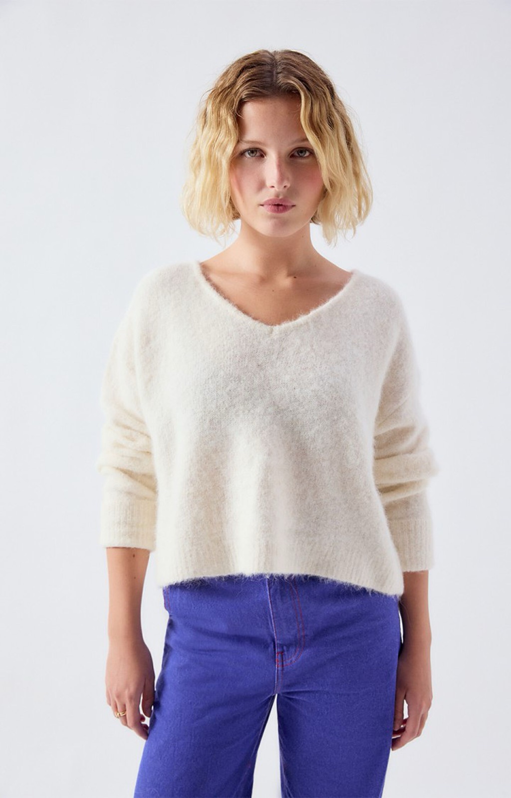 Pull femme East d'American Vintage en maille nacre chinée, col V, porté avec un pantalon bleu électrique