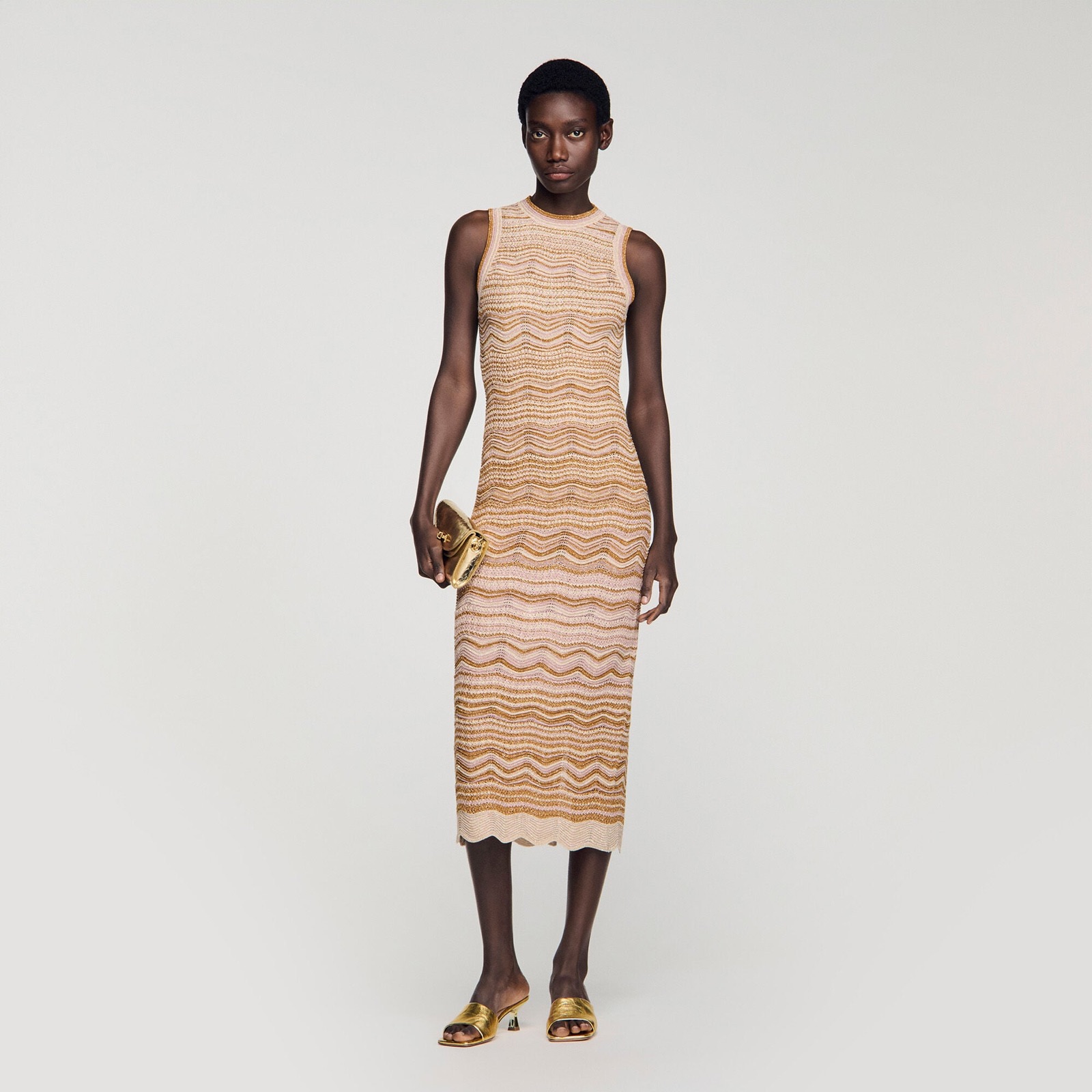 Robe longue sans manches en maille fantaisie Sandro, dégradé rose poudré et doré à motif ondulé, portée avec mules dorées