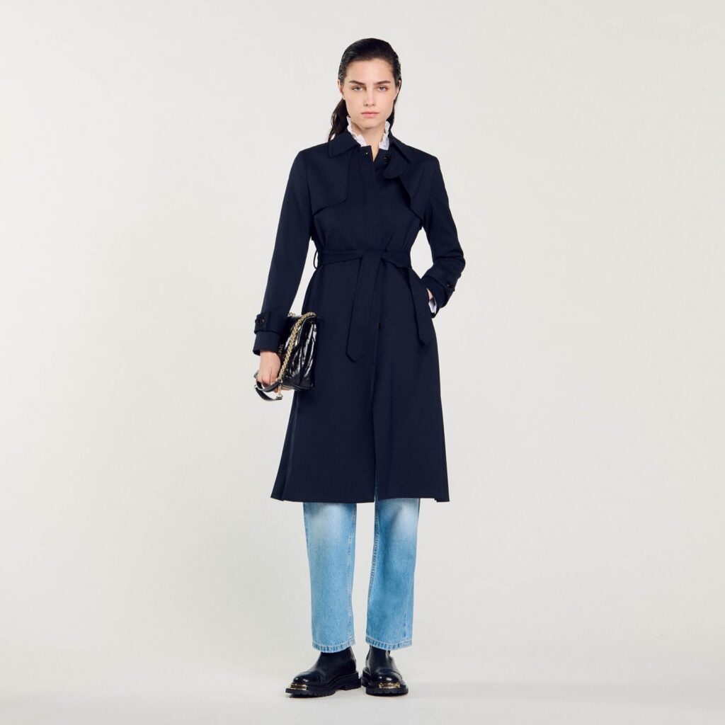 Manteau en laine bleu marine Sandro, ceinture nouée, porté avec un jean clair et des boots noires