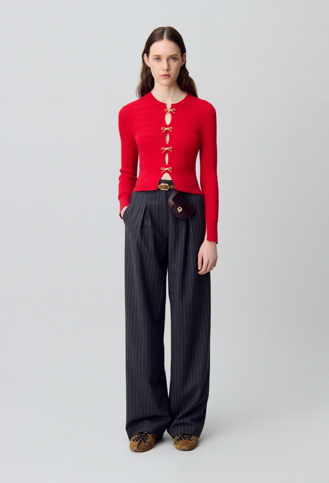 Pull rouge Manivelle de Claudie Pierlot en maille fine côtelée, fermé par des nœuds en cordage doré, porté avec un pantalon à fines rayures
