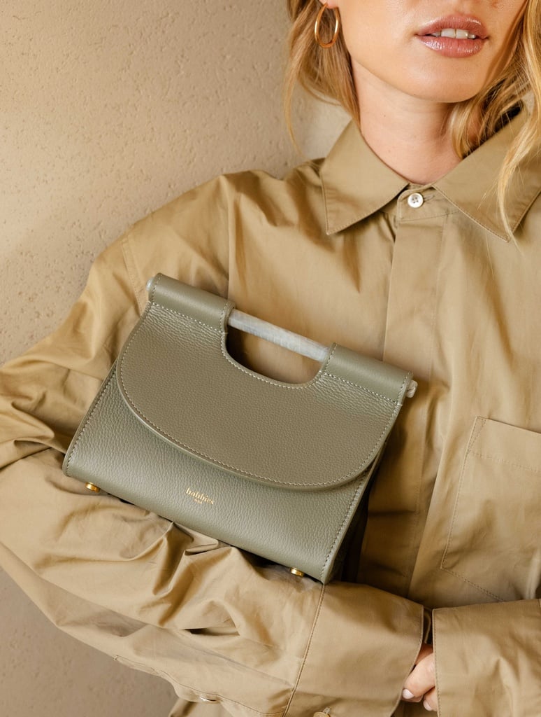 Sac Ancone Mini de Bobbies en cuir graine vert Esterel, porte a la main sur une chemise taupe