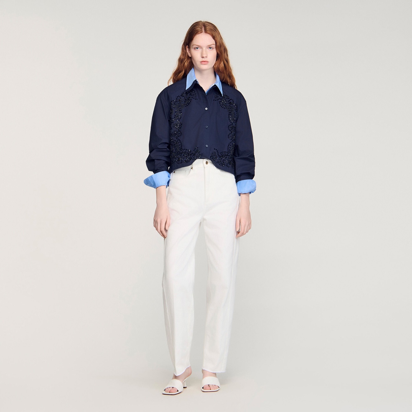Chemise courte en coton marine a broderie fleurie, portee sur une chemise bleu ciel et un jean blanc, Sandro