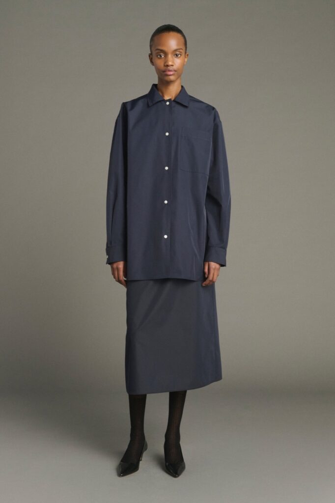 Jupe Lili en toile technique bleu marine, coupe évasée mi-mollet, portée avec une chemise marine et des escarpins noirs, par Soeur