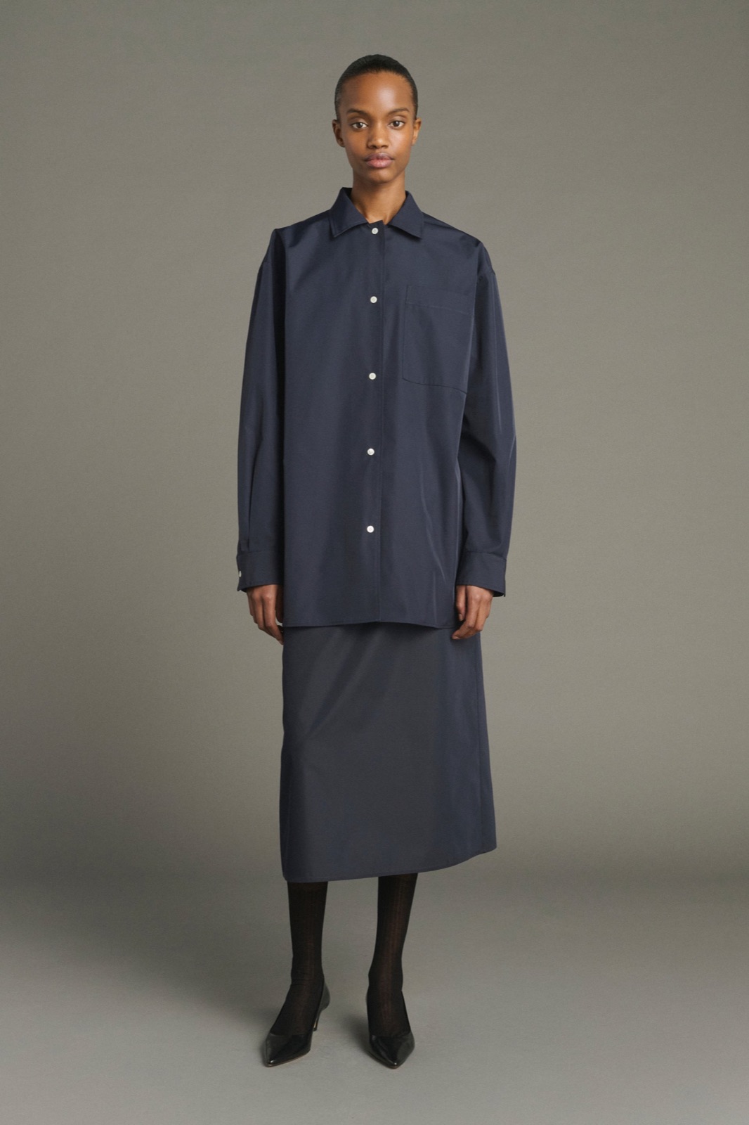 Jupe Lili en toile technique bleu marine, coupe évasée mi-mollet, portée avec une chemise marine et des escarpins noirs, par Soeur
