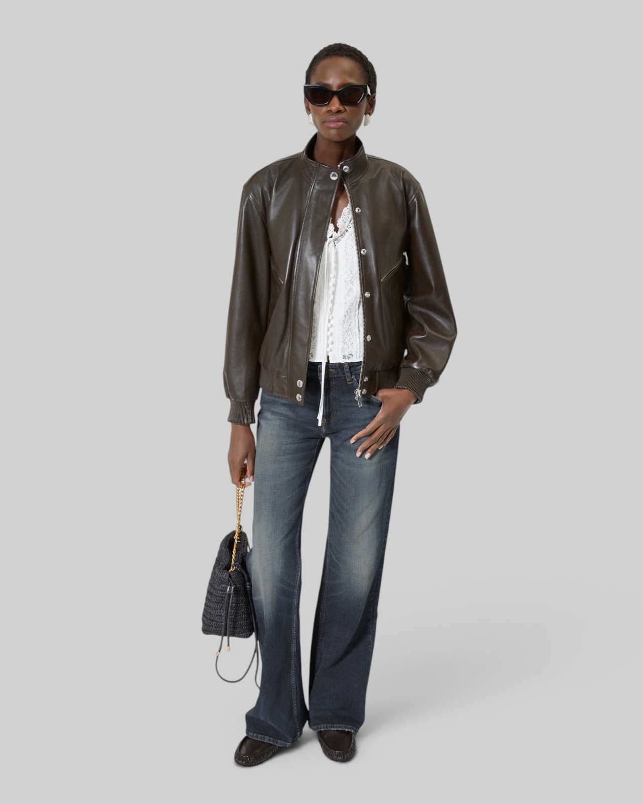 Blouson en cuir marron à col montant de The Kooples, porté ouvert sur un haut en dentelle blanche et un jean flare