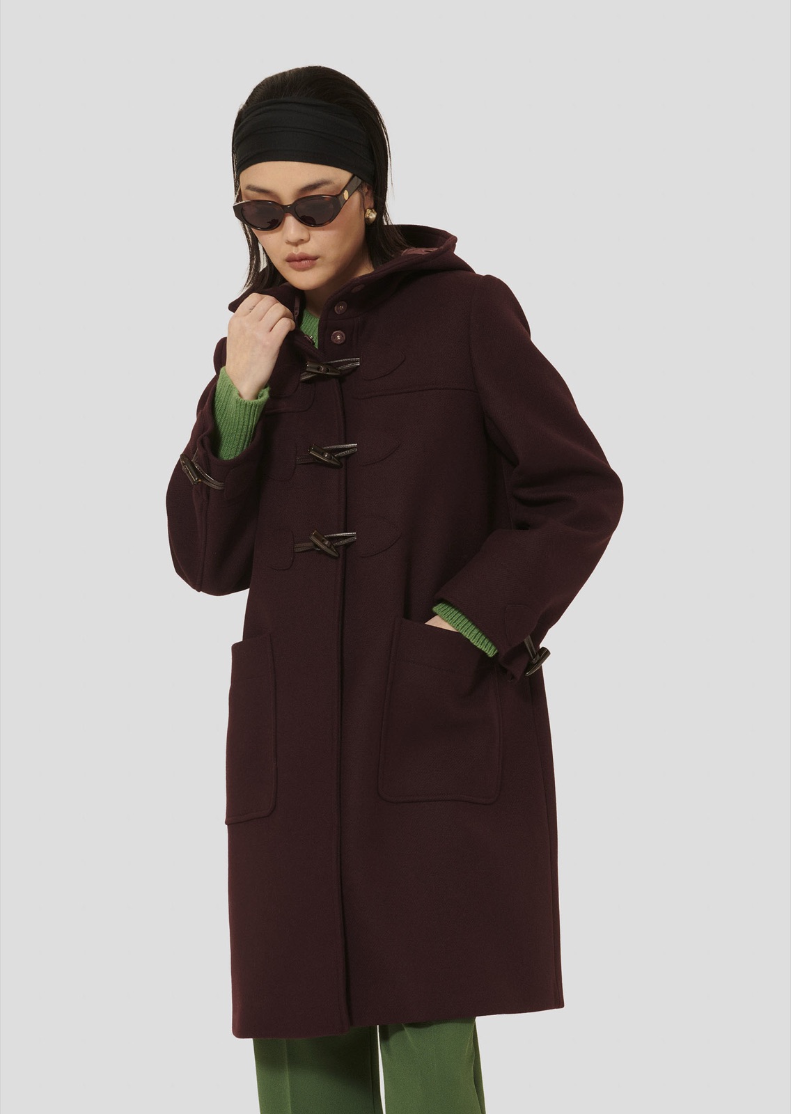 Duffle-coat Manoela de Tara Jarmon en laine figue, capuche et fermetures brandebourg, porté sur un pull et un pantalon verts