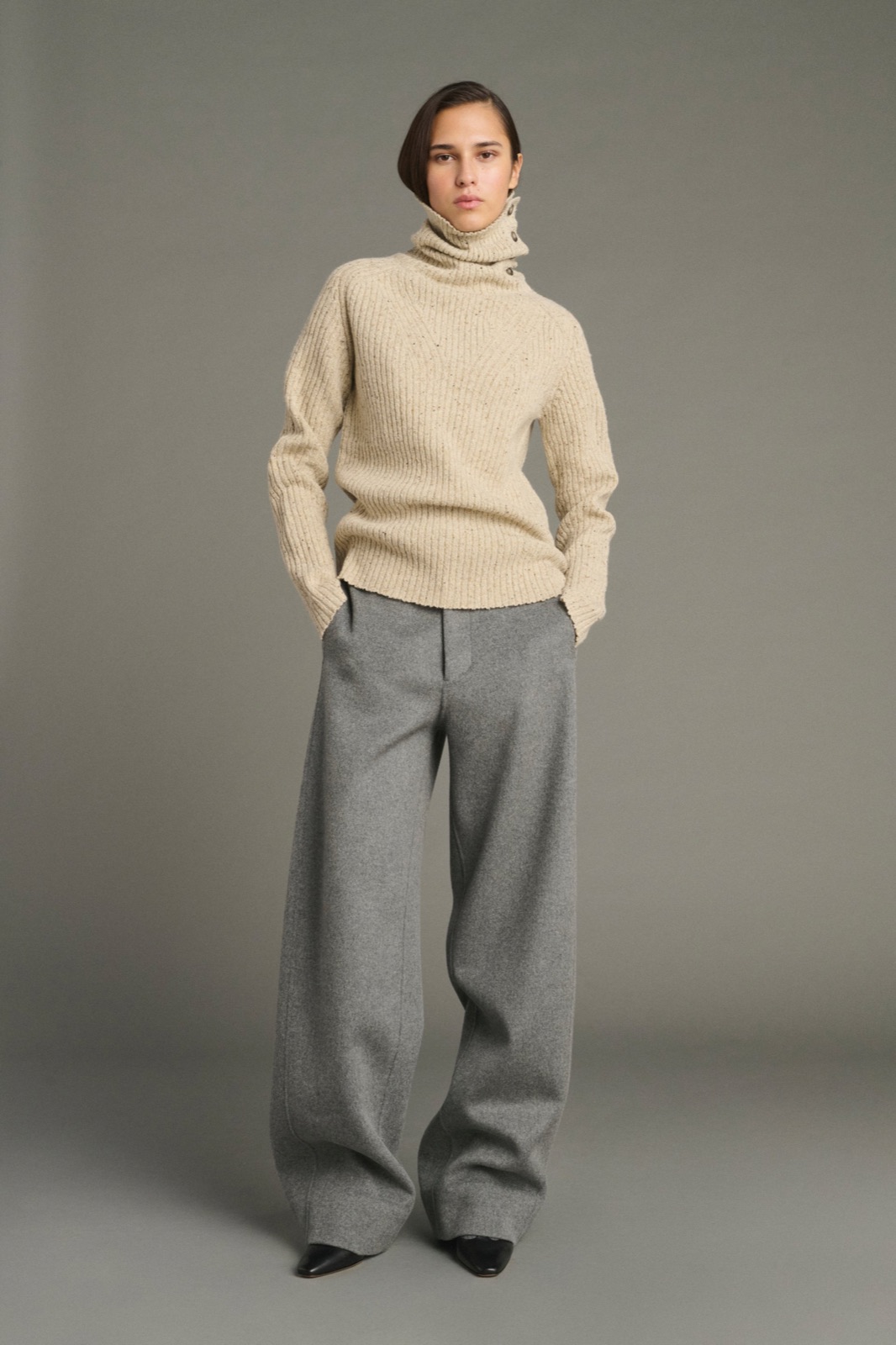 Pull Joey beige clair en laine Donegal mouchetée de Soeur, col montant boutonné sur le côté, porté avec un pantalon large gris