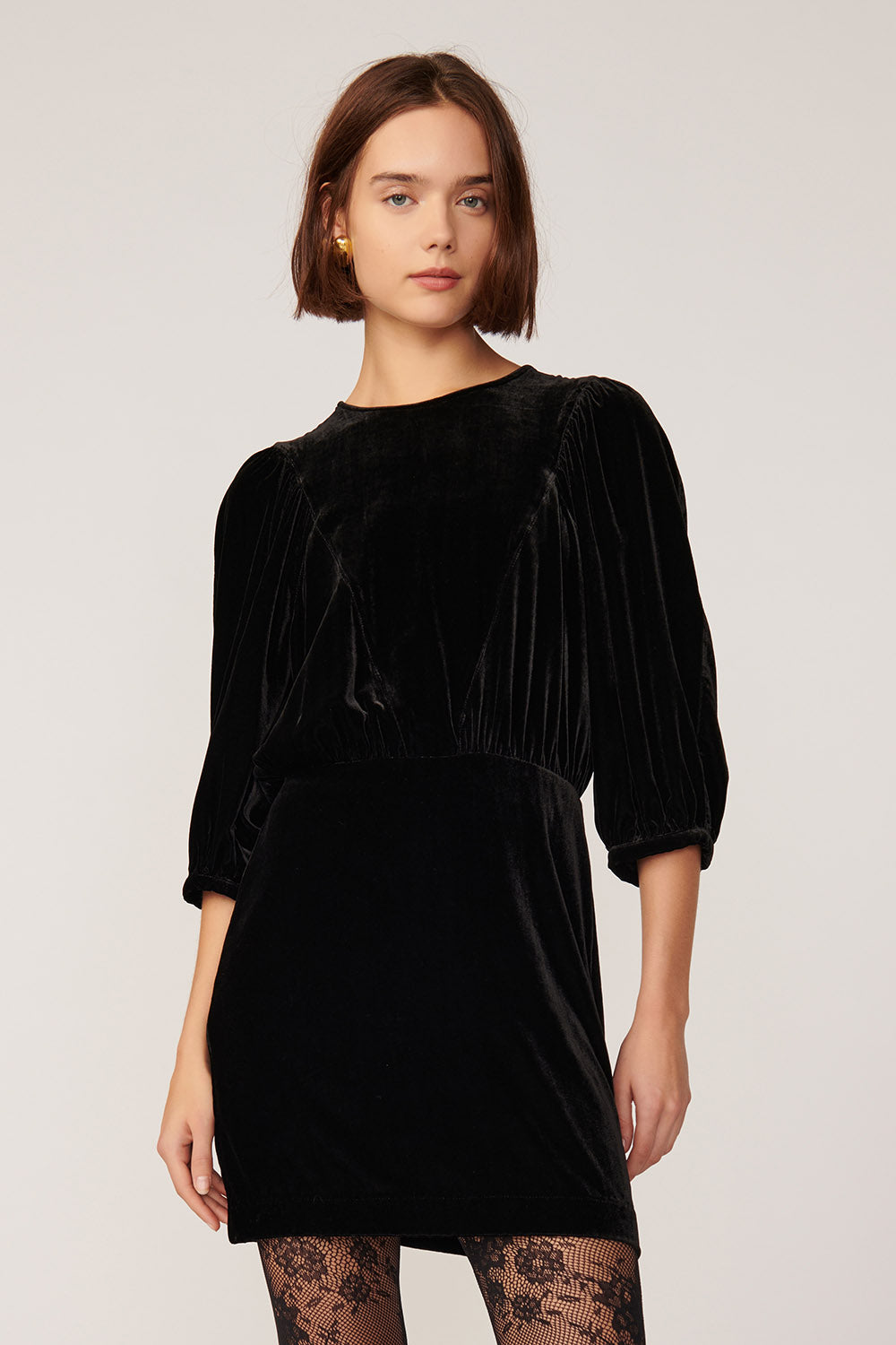 Robe courte en panne de velours noire Landria de Des Petits Hauts, manches ballon mi-longues et col rond, portee avec des collants en dentelle